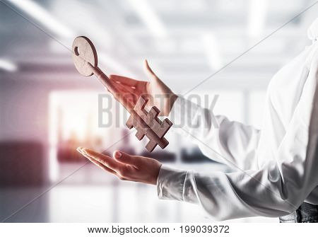 Business woman in white shirt keeping big stone key in hands with office view and sunlight on background. Mixed media.