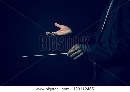 Orchestra conductor hands Musician director holding stick on dark background