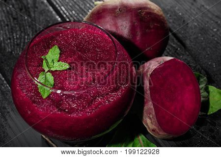 A close-up picture of bright red beet smoothie in a glass on a black table background. Juicy beetroots with fresh salad leaves and green decorative mint. Detoxification and dietary concept.