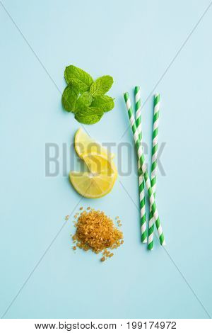 Mojito ingredients. Lemon, mint and cane sugar blue background. Sweet sugar, mint leaves, lemon and striped straw.