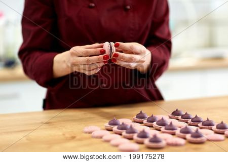 cooking, confectionery and food concept - chef sandwiching baked macarons shells with cream together at pastry shop
