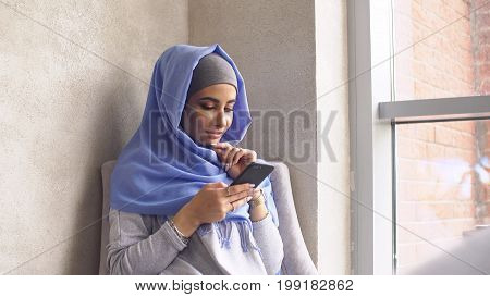 Beautiful Muslim Girl Using Smartphone in Cafe. Modern Muslim Woman and New Technologies