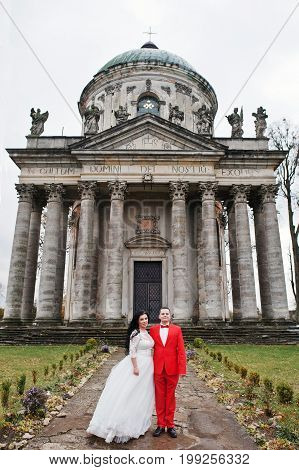 Wedding Couple Hugging Against Baroque Chucrh In The Background.