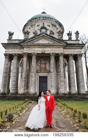 Wedding Couple Hugging Against Baroque Chucrh In The Background.