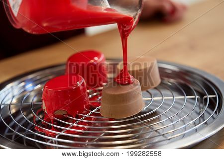 cooking, baking and food concept - jug pouring glaze to chocolate cakes on tray with grid at pastry shop