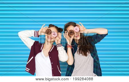 people, teens and fast food concept - happy smiling pretty teenage girls or friends with donuts making faces and having fun over blue ribbed background