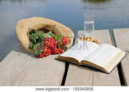 Red berries viburnum on a wooden table in a straw hat with a book of the Bible