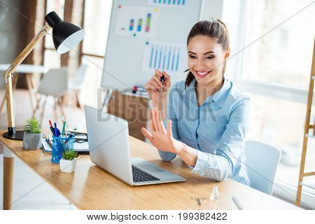 Cropped close up photo of young lady secretary in blue formal wear filing her nails at her work place on a desktop smiling