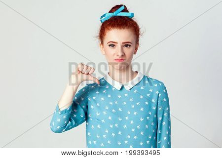 Young beautiful unhappy girl with blue dress showing thumb down. Studio shot on light gray background.