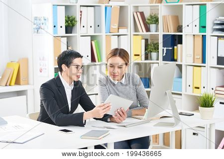Multi-ethnic group of talented interior designers gathered together at office desk and discussing joint project, they using digital tablet