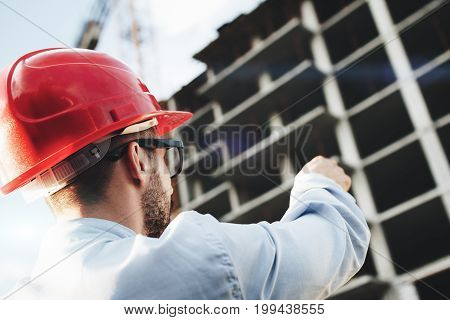 Architect Or Safety Officer In Red Hard Hat On Background Of Construction Site. Engineer Builder Man