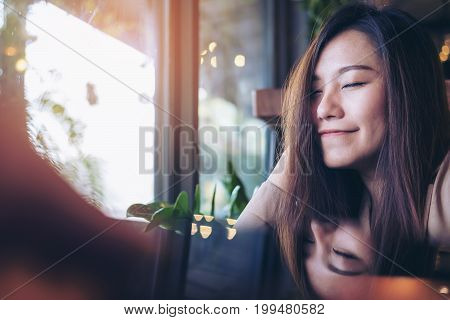 A beautiful asian woman close her eyes and enjoy relaxing time in modern cafe with reflection on table