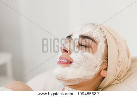 Spa beauty organic facial mask application at day spa salon. Woman applying facial clay mask at spa salon side view.