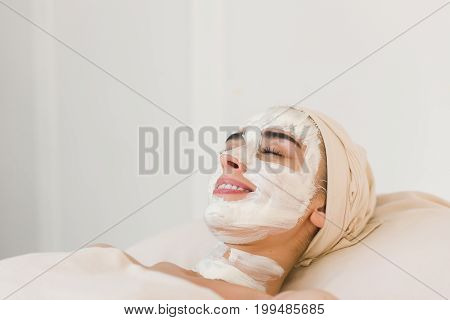 Spa beauty organic facial mask application at day spa salon. Woman applying facial clay mask at spa salon side view.