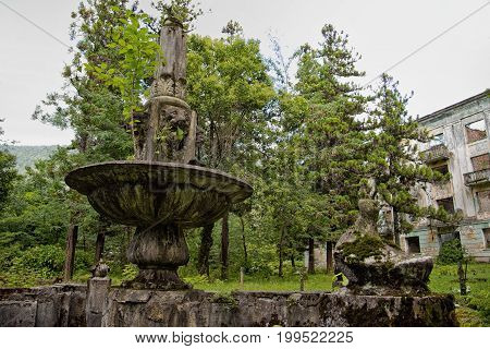The abandoned miner's ghost town Tquarchal (Tkvarcheli, Abkhazia). Idle fountain with lion's head on the background of a ruined house.