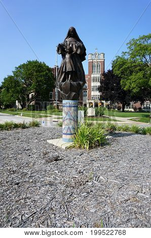 JOLIET, ILLINOIS / UNITED STATES - JULY 17, 2017: A sculpture of Mother Mary Alfred Moes, O.S.F., assisting a child, stands on a mosaic pedestral, in a traffic island, in front of the University of Saint Francis.