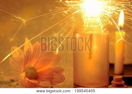 Concept Of Sparklers In Glass Jar At Night And Fresh Yellow Flower With Blurred Golden Light Candle