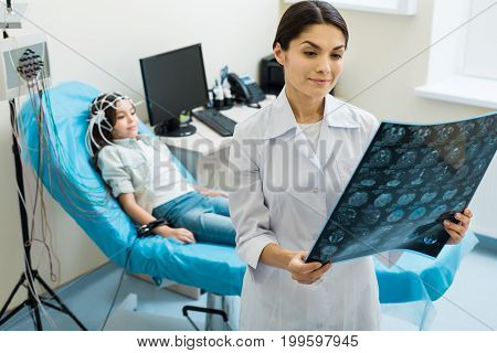 Being thorough. Beautiful young female doctor looking through the results of computer tomography while conducting electroencephalography of a little girl