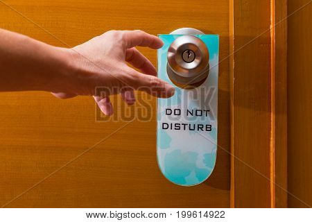 male hand reaching to metal door knob with old Do Not Disturb sign tag haning on concept of needing privacy or privacy about being intruded