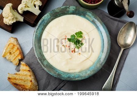 Vegetarian white soup cream from cauliflower in a vintage ceramic plate on a light concrete background. Selective focus. top view. Copy space.