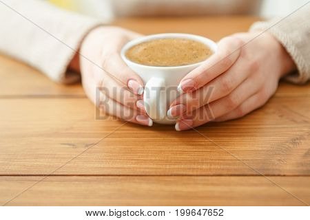 Female holding a cup of coffee while sitting at wooden table, shallow depth of field.