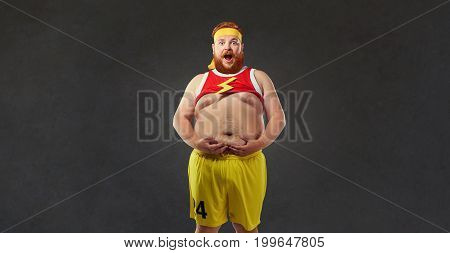 Fat man in sports clothes is holding his stomach. Humor sport concept.