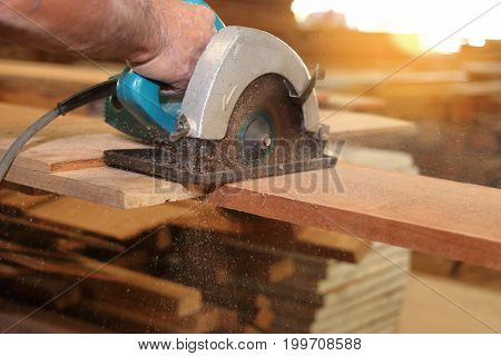 Electric circular saw is being cut a piece of wood by carpenter in carpentry workshop.