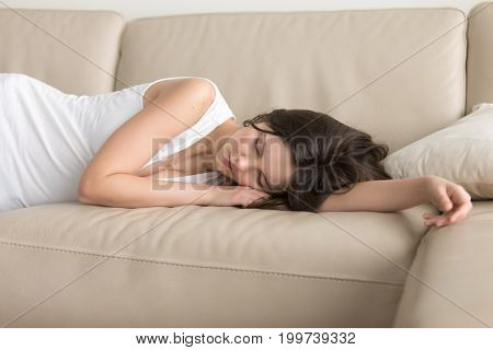 Young woman lying asleep on couch, sleeping attractive girl taking nap at home, resting on arm on comfortable sofa, exhausted teenager dozing after sleepless night, feeling lack of sleep deprivation