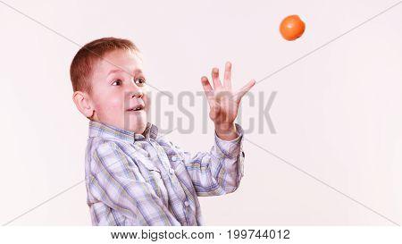 Nature and free time prankster little boy. Child have fun with wooden sling shot and fruit aim orange.
