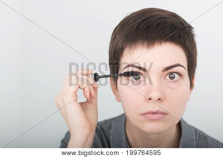 Beauty make-up. Portrait of young girl with fake eyelashes applying black mascara on lashes, holding brush in hand. Sexy female with soft skin and perfect makeup. Cosmetics.