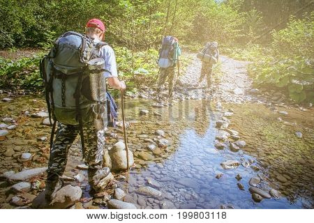 Ford river. Three travellers with backpacks have adventures