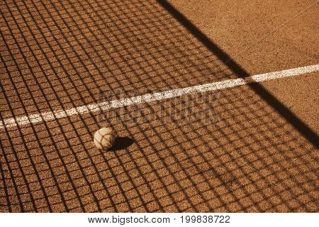 A tennis ball lies on the court in the shadow mesh