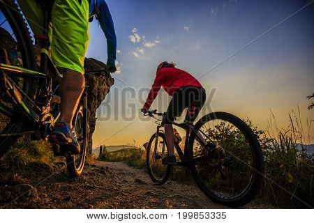 Mountain biking women and man riding on bikes at sunset mountains forest landscape. Couple cycling MTB enduro flow trail track. Outdoor sport activity.