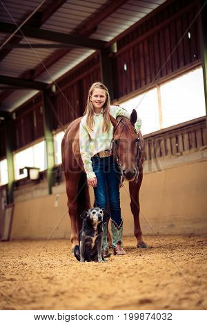 Young Cowgirl With Her Horse And Dog in indoors riding arena
