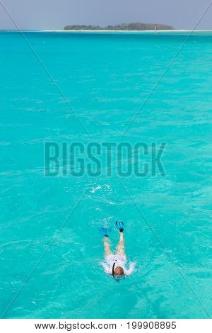 Woman snorkeling in clear shallow sea of tropical lagoon with turquoise blue water and coral reef, near exotic island. Mnemba island, Zanzibar, Tanzania.