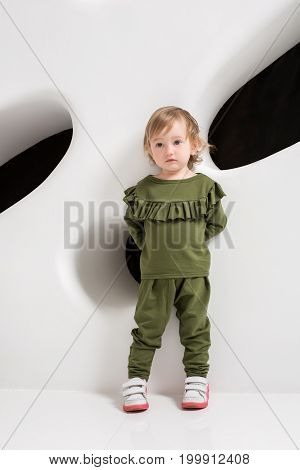 Year-old child standing near white wall in studio. Portrait of cute girl posing in studio.