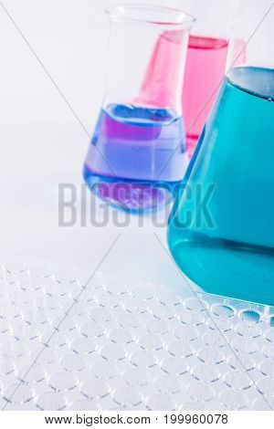research, science and clinic background. 96 well micro plate and  laboratory beakers with colorful liquids and reagents.
