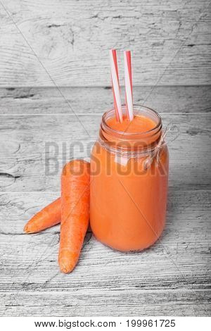 A mason jar full of carrot milkshake or smoothie with drinking straw on a gray wooden background, close-up. Bottle of fresh carrot juice with two whole carrots. Sweet carrot juice. Vegetable concept.