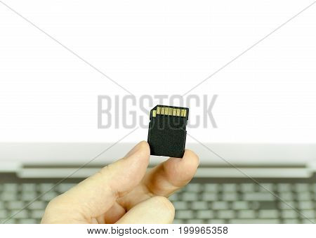 Close-up view of a hand holding a black SD memory card with a laptop isolated in white background