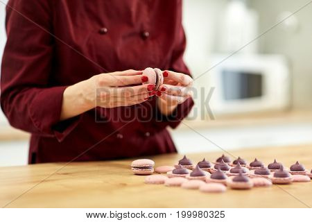cooking, baking, confectionery and food concept - chef sandwiching baked macarons shells with cream together at pastry shop kitchen