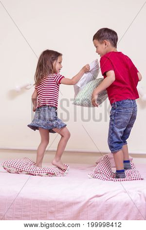 Kids Concepts and Lifestyle. Small Caucasian Kids Having a Funny Pillow Battle on Bed Indoors. Vertical Image Composition