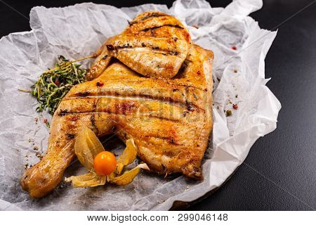 Grilled Chicken Tabaka Served With Herbs On Black Background.