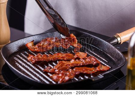 Young Woman In A Gray Apron Fries Bacon