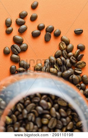 Close-up Top View Of Roasted Coffee Beans In A Glass Cup On An Orange Background. Vertical Photograp