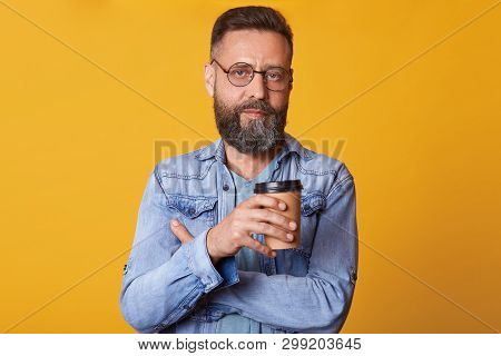 Indoor Studio Shot Of Magnetic Successful Man Standing Isolated Over Bright Yellow Background, Havin