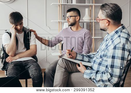 Young Man In Glasses Comforting His Depressed Friend During Meeting With Counselor