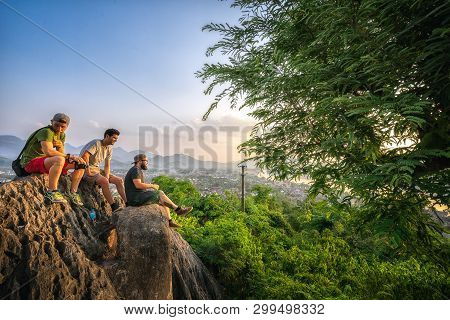 Luang Phabang, Laos - May 8, 2017: Tourists Sitting On A Rock And Admiring The Mountain Landscapes. 