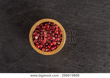 Lot Of Whole Dry Peruvian Pink Pepper In A Wooden Bowl Flatlay On Grey Stone