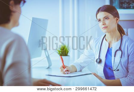 Doctor and patient discussing medical problems in a hospital consulting room. Doc filling in a patient's form