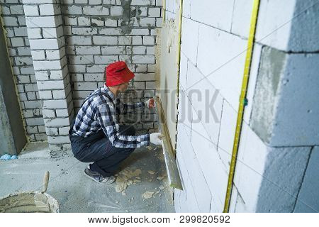 High Angle Shot Of Builder Sitting On His Hunkers Plastering On Block Wall